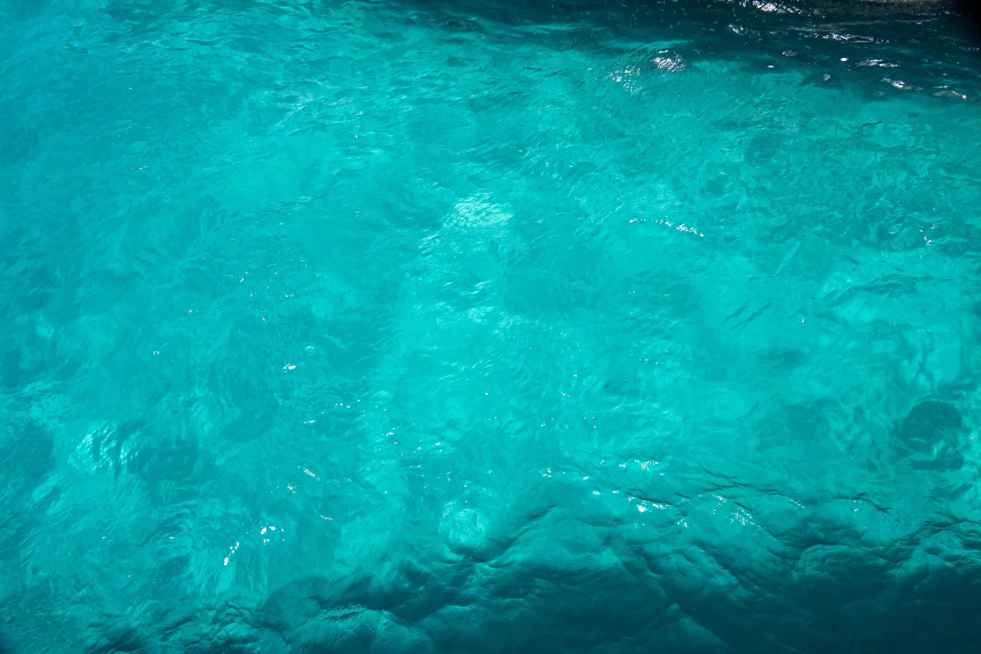 この写真はマルタで撮影された、鮮やかなターコイズブルーの海の表面を捉えたものです。水面は穏やかに波打ち、光の反射がキラキラと輝いています。水の色は非常に透明度が高く、海底の様子が透けて見える箇所もあります。全体的に、静かで穏やかな、そして南国らしい美しい雰囲気が漂っています。波の動きによって生じる光と影のコントラストが、水面の美しさを際立たせています。写真の右上が少し暗くなっていることから、撮影場所が日陰になっている可能性を示唆しています。
