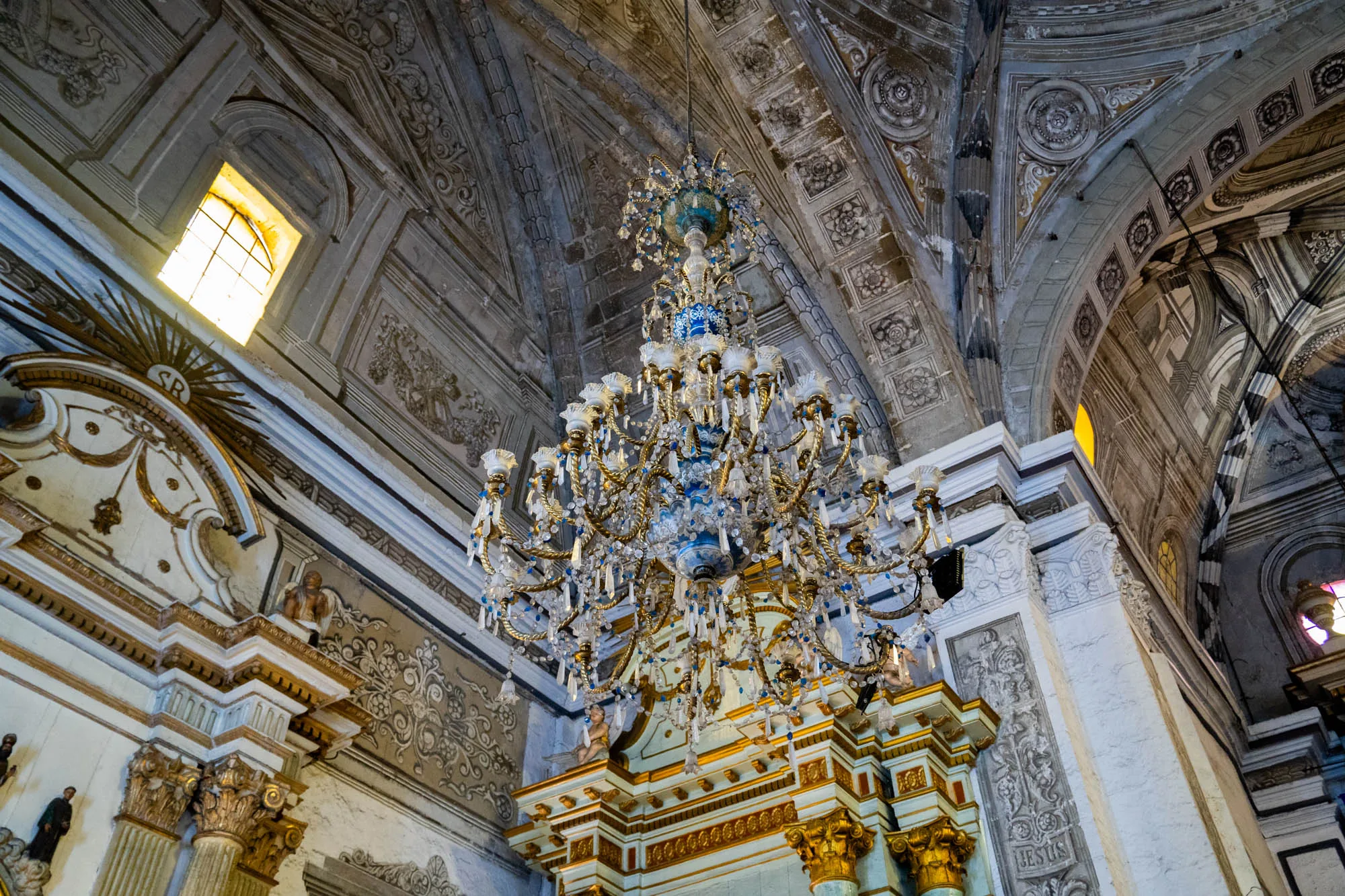 フィリピンのマニラで撮影された写真は、教会の内装を捉えています。特に目を引くのは、豪華なシャンデリアです。シャンデリアは、金色の装飾と青色のアクセントが施され、無数のクリスタルが吊り下げられています。光を受けて輝き、非常に華やかです。天井は高く、複雑な装飾が施されています。石造りの壁には彫刻が施され、歴史を感じさせます。窓からの光が差し込み、空間を明るく照らしています。全体的に、荘厳で神聖な雰囲気を醸し出しています。建物の建築様式や装飾から、歴史的な建造物であることが伺えます。細部にまでこだわりが見られ、美しい写真です。